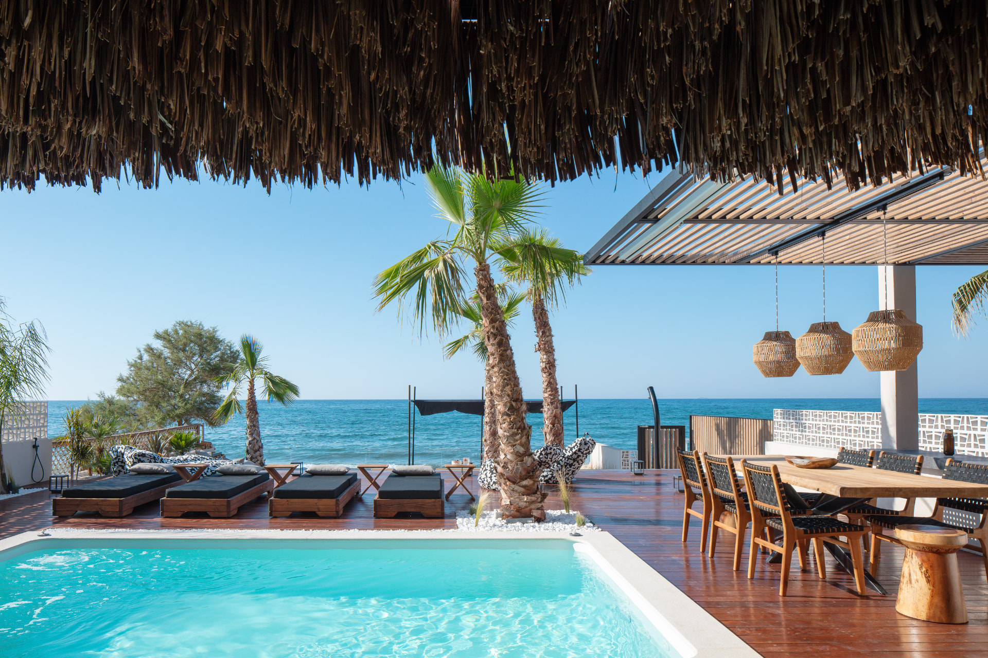 Dining pergola with wooden table, sunbeds and the sea beyond
